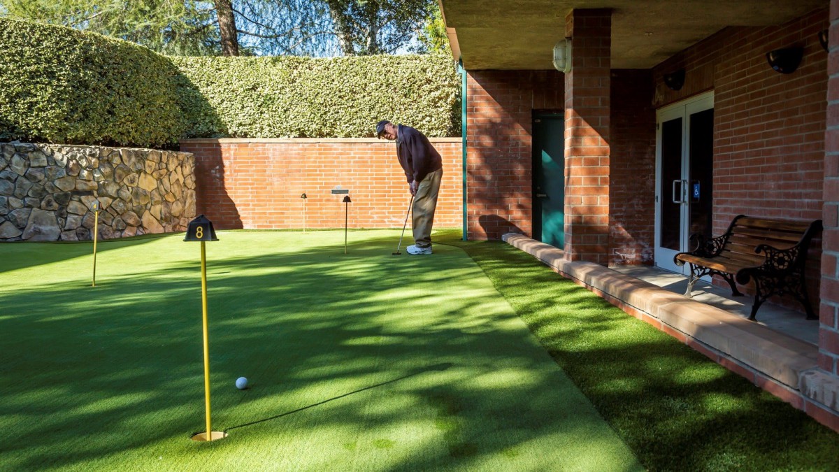 A man practicing his putting skills in an outdoor garden setting.