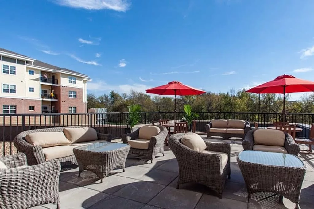 A spacious outdoor patio area with wicker furniture and red umbrellas under a clear blue sky.