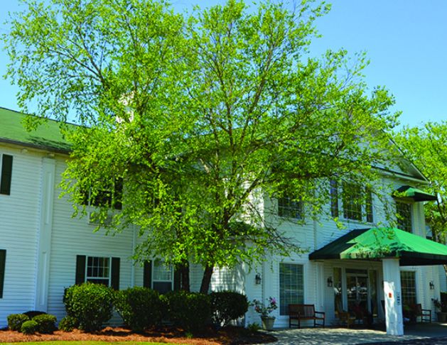 A white two-story building with a large tree in front and a green awning.