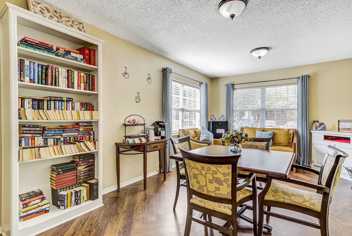 A cozy living and dining area with a bookshelf, cushioned chairs, and large windows.
