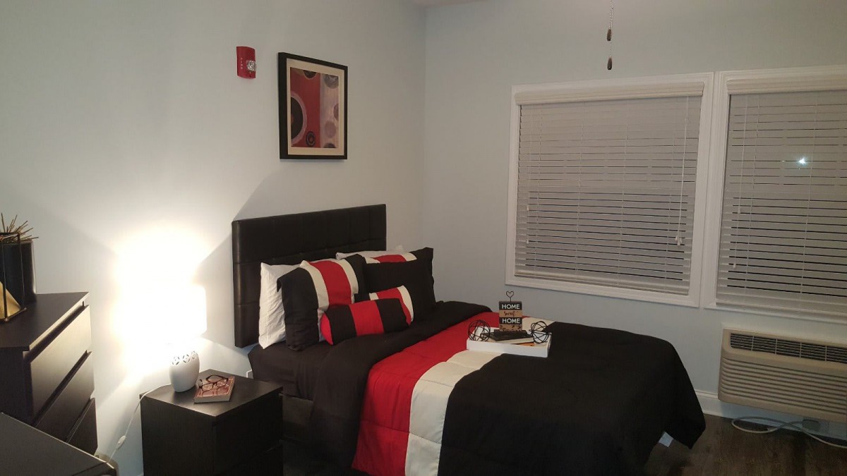 A modern bedroom with a stylish black and red bedding set, featuring a framed artwork on the wall and a nightstand with a lamp.