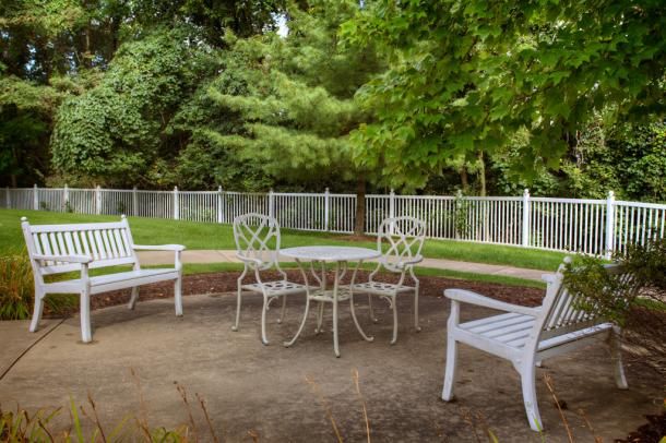 A peaceful outdoor patio area with white furniture surrounded by lush greenery.