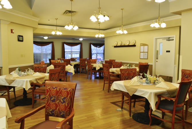 A cozy dining room with neatly arranged tables and chairs, featuring warm lighting.