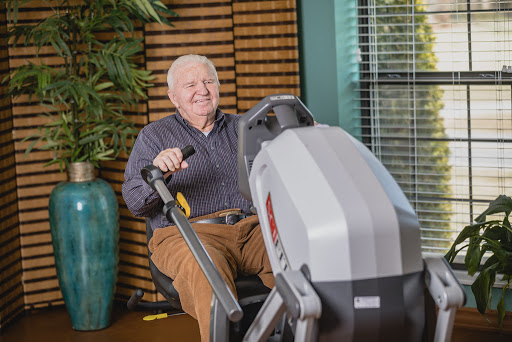 An elderly man engages in a workout using exercise equipment in a comfortable indoor environment.