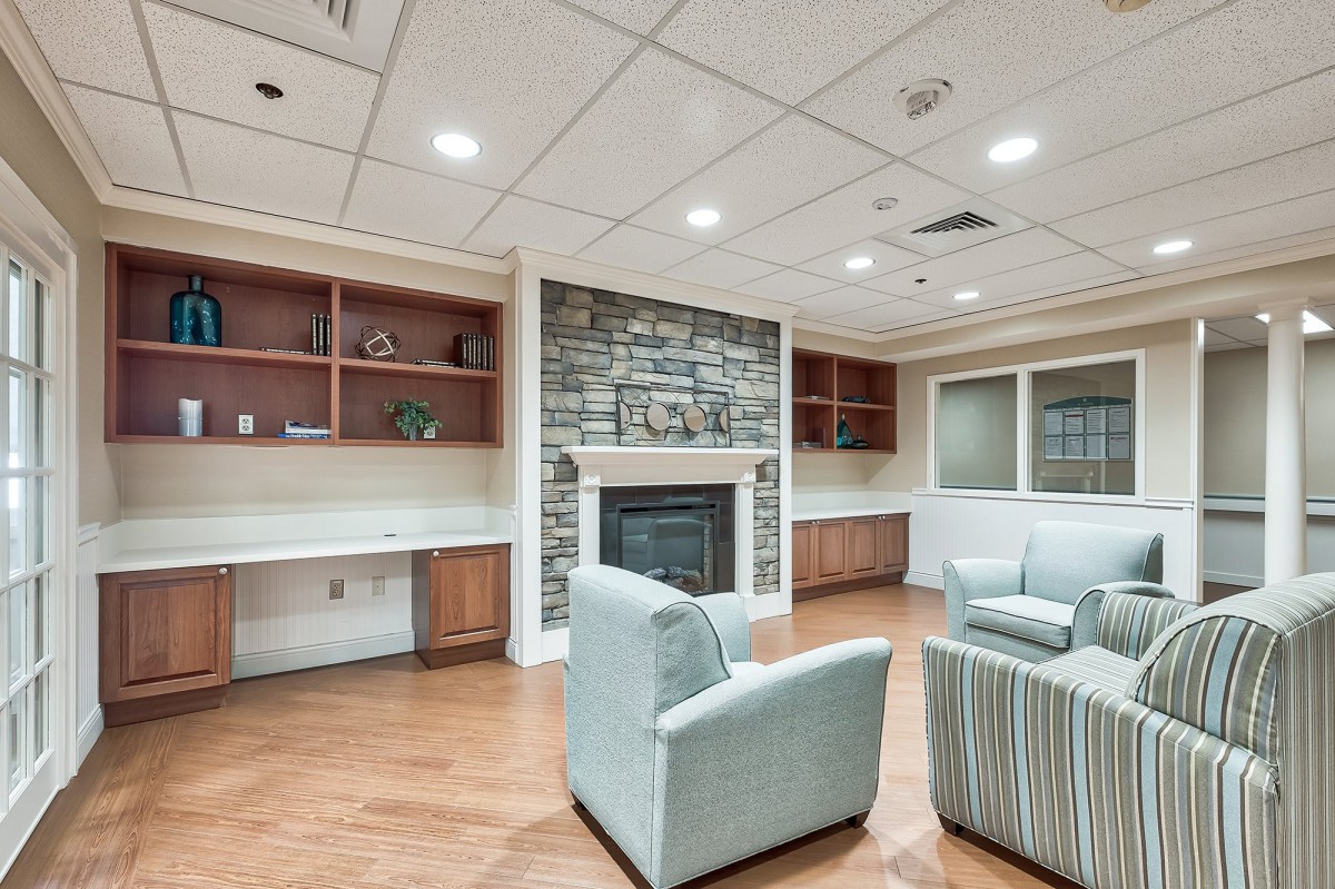 A cozy living room with a stone fireplace, surrounded by comfortable armchairs and built-in wooden shelves.