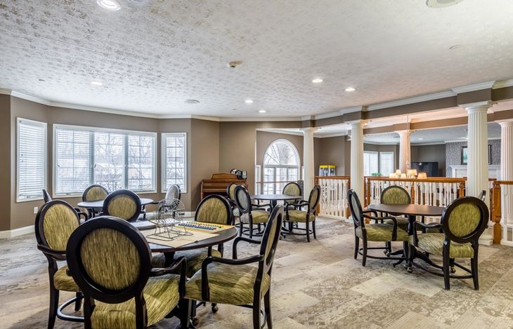 A well-lit dining area with elegant chairs and tables, featuring large windows and a carpeted floor.