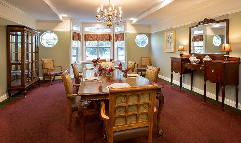 A traditionally decorated dining room with a wooden table and chairs, illuminated by a chandelier.