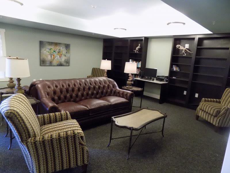 A cozy living room featuring a leather sofa, striped armchair, coffee table, and bookshelves.