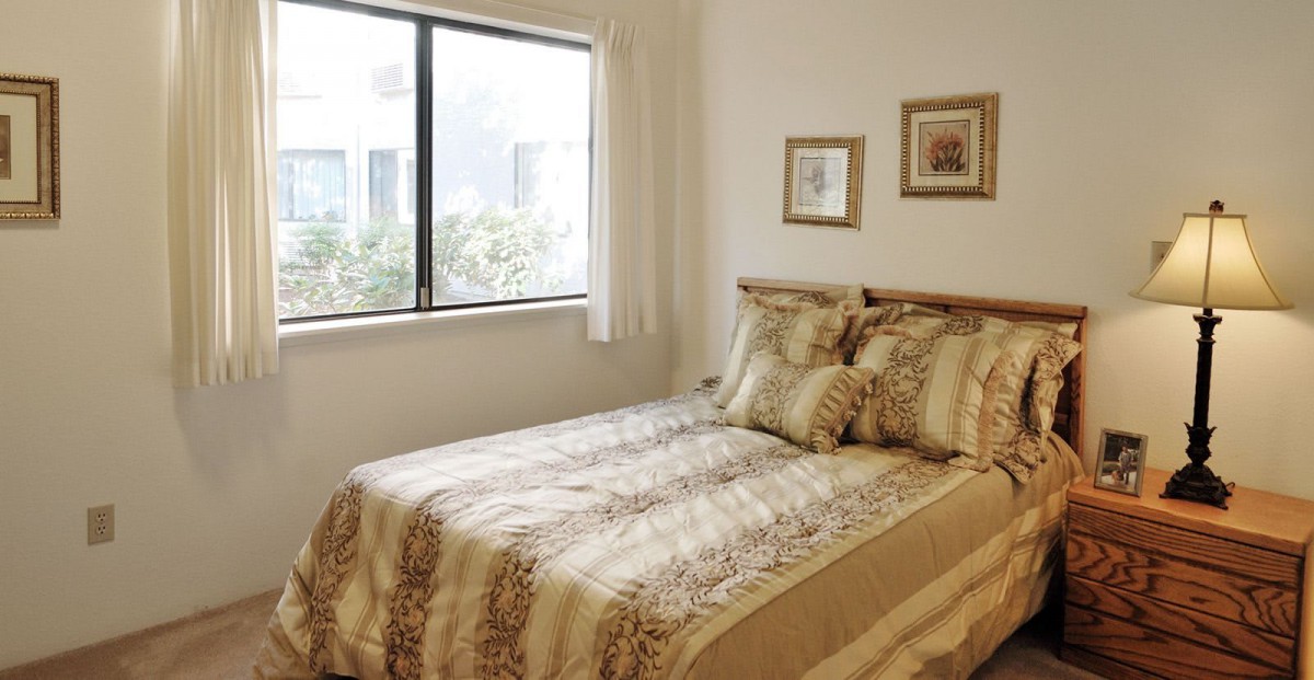 A cozy bedroom with a neatly made bed and decorative pillows, featuring two framed pictures on the wall and a large window with curtains allowing natural light.