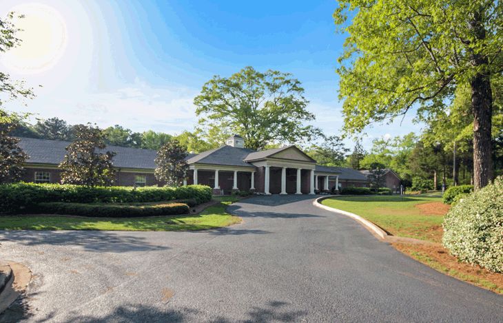 A large residential house with a circular driveway and surrounding greenery.