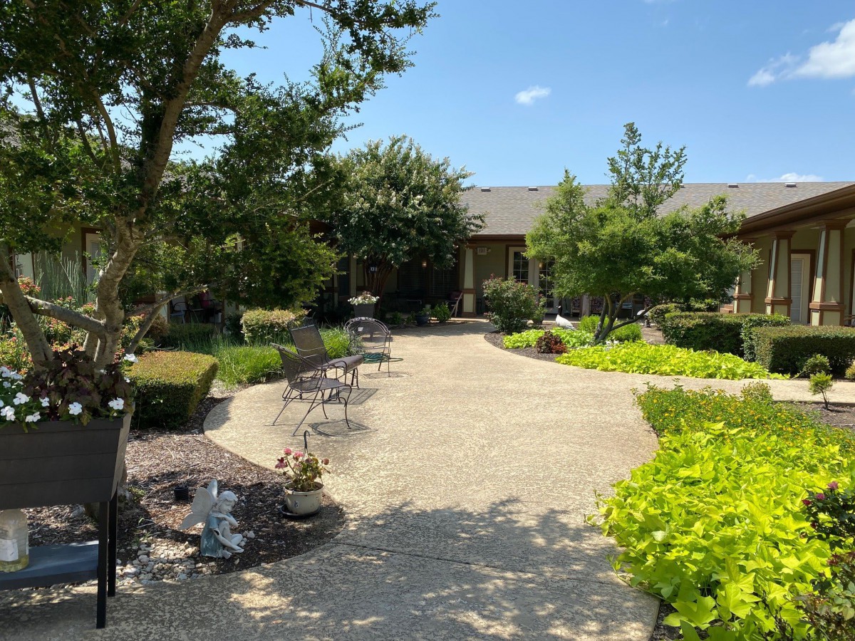 A beautiful garden with a paved pathway and seating surrounded by lush greenery under a clear blue sky.