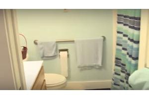 A small bathroom featuring a toilet, a towel rack with towels, and a toilet paper holder against a light blue wall.
