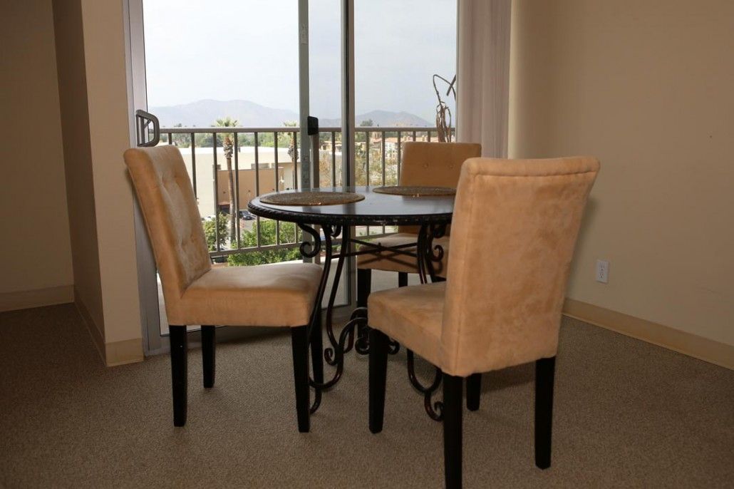 Dining area with a round table and chairs near a glass door overlooking a balcony.