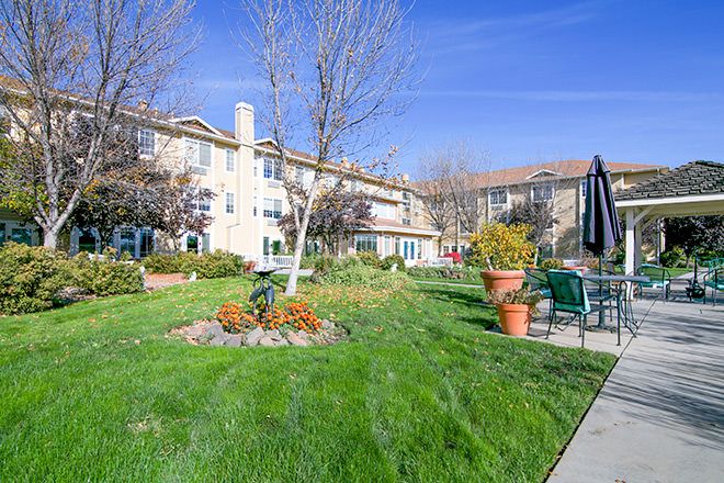 A well-maintained garden area in front of an apartment building with lush green grass, trees, and potted plants.