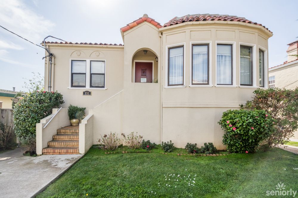 A Spanish-style stucco house with a manicured lawn and arched entryway.