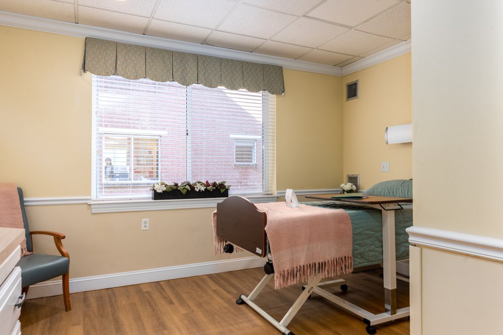 A hospital room with a medical bed, featuring a window with curtains and a wooden floor.