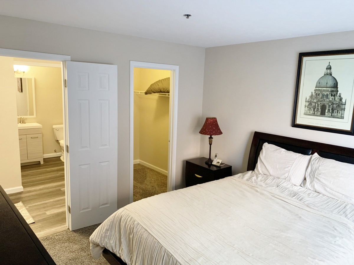 A minimalist bedroom featuring a bed, nightstand with lamp, and an open closet.