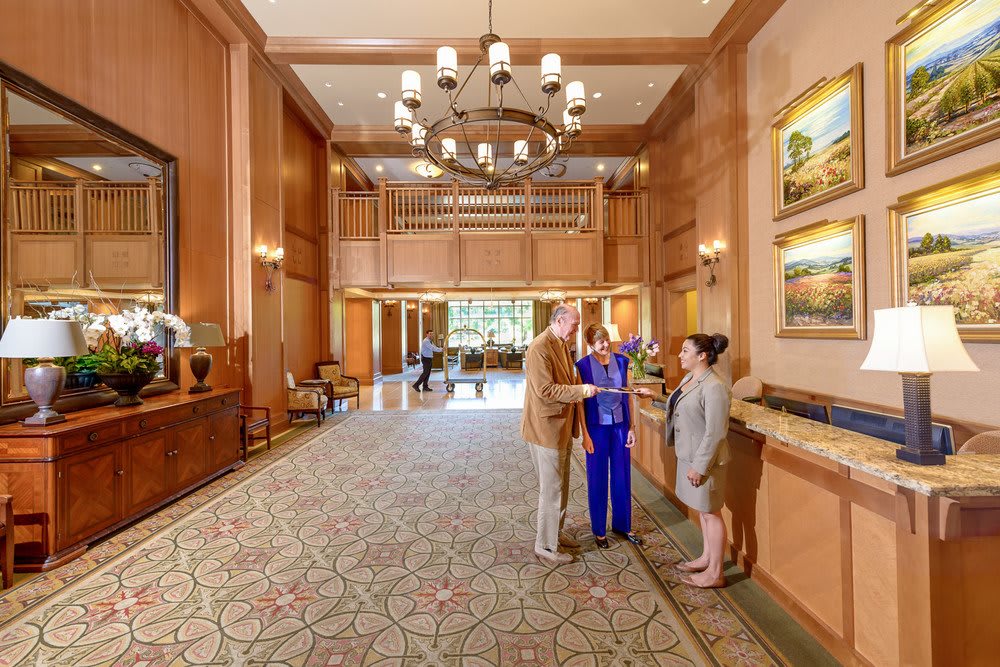 A hotel lobby with people conversing near the reception desk.