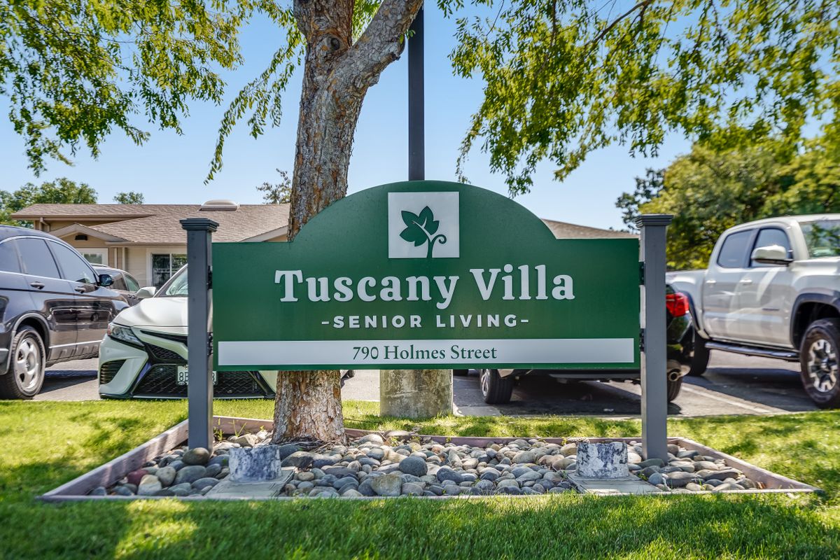 A sign for Tuscany Villa Senior Living surrounded by trees and greenery.