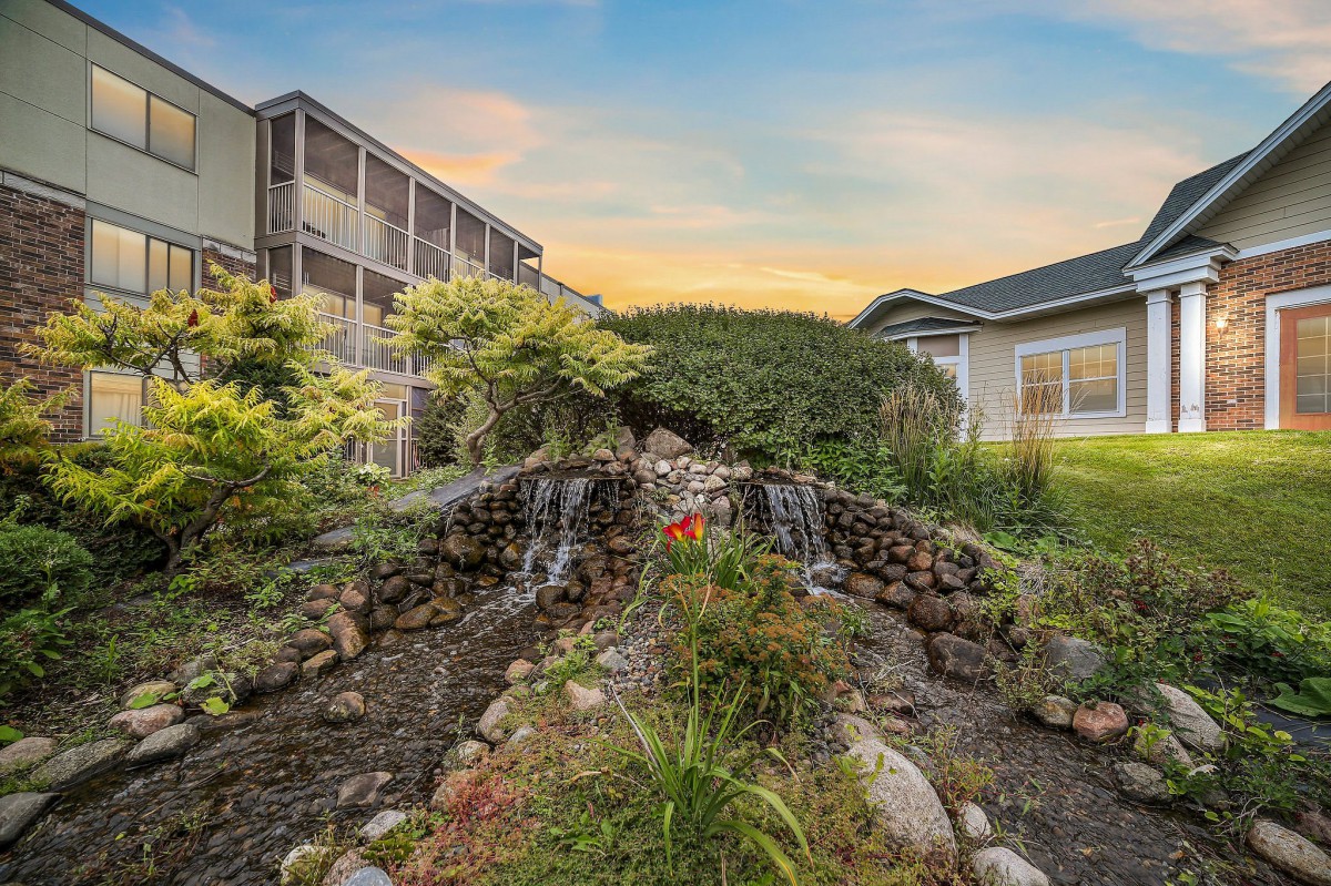 A serene garden featuring a small waterfall between buildings at sunset.