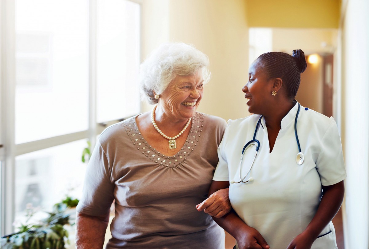 A nurse walking and talking with a senior woman in a healthcare setting.