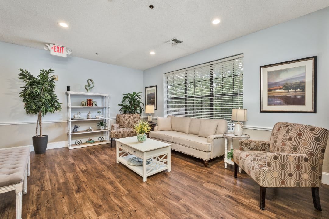 A cozy living room with modern furniture and decor, featuring a sofa, armchairs, coffee table, and bookshelf on wooden flooring.
