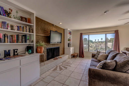 A cozy living room featuring a television, bookshelves, and natural light from a large window.
