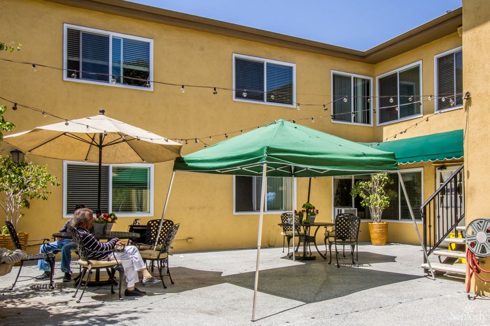 A sunny outdoor patio area with tables, chairs, and canopies in front of a building.