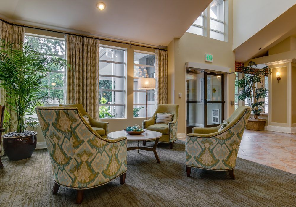 A cozy hotel lobby featuring patterned chairs, a round table, and large windows.