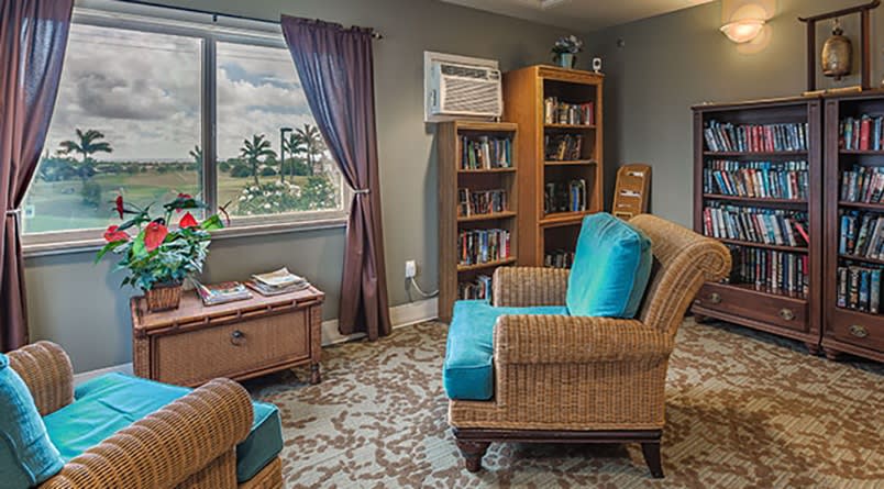A cozy living room with an armchair, bookshelf, and a window offering a scenic view.