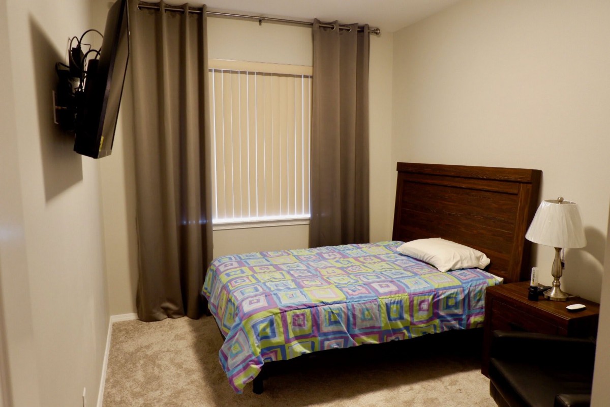 A neatly arranged bedroom with a single bed, curtains, and window blinds.