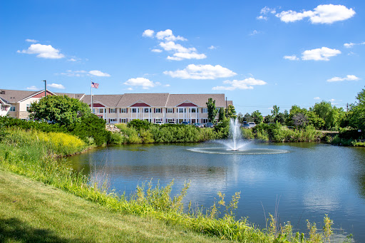 A serene landscape featuring a building by a pond with a fountain, under a clear blue sky.