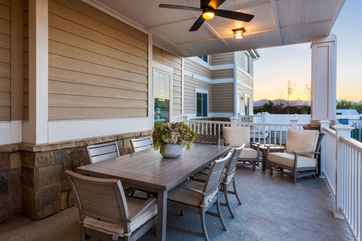 A cozy outdoor patio area with a dining table, chairs, and a fan under a covered deck during sunset.