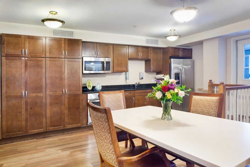 A modern kitchen and dining area featuring wood cabinets, stainless steel appliances, and a table with flowers.