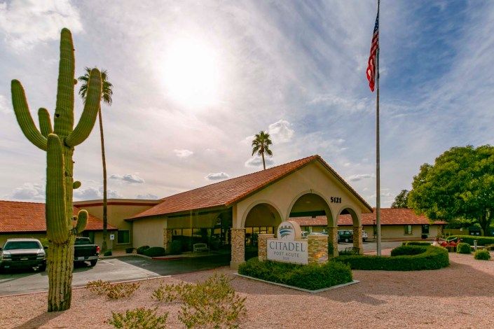 A sunny day at the entrance of a building with palm trees and a flag.