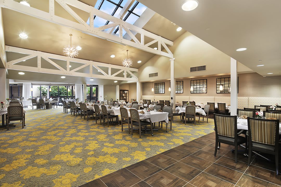 A spacious dining area with tables and chairs, featuring large windows and ceiling beams.