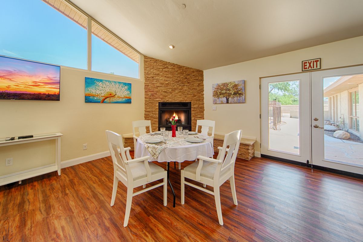 A cozy dining room with a round table set for four, featuring a warm fireplace and bright natural lighting.