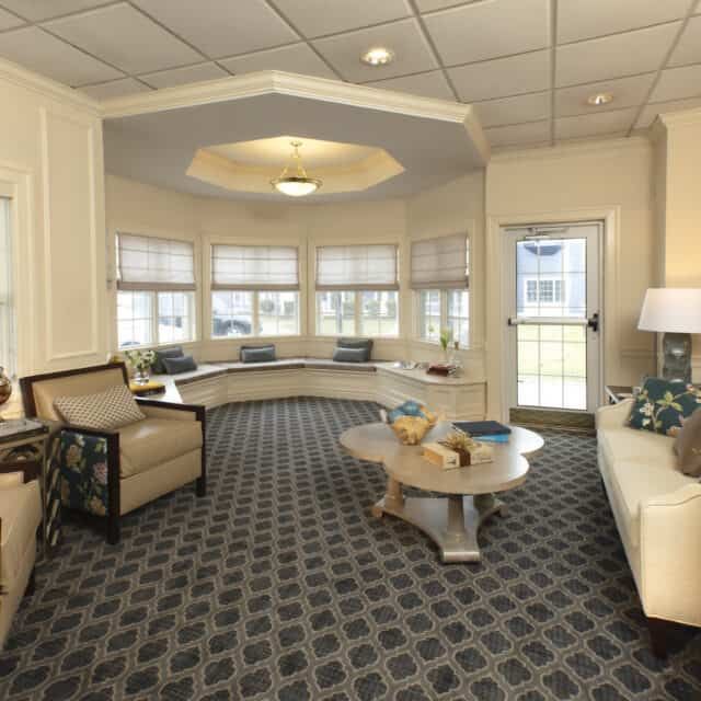 A cozy living room with comfortable seating, a patterned carpet, and large windows providing ample natural light.