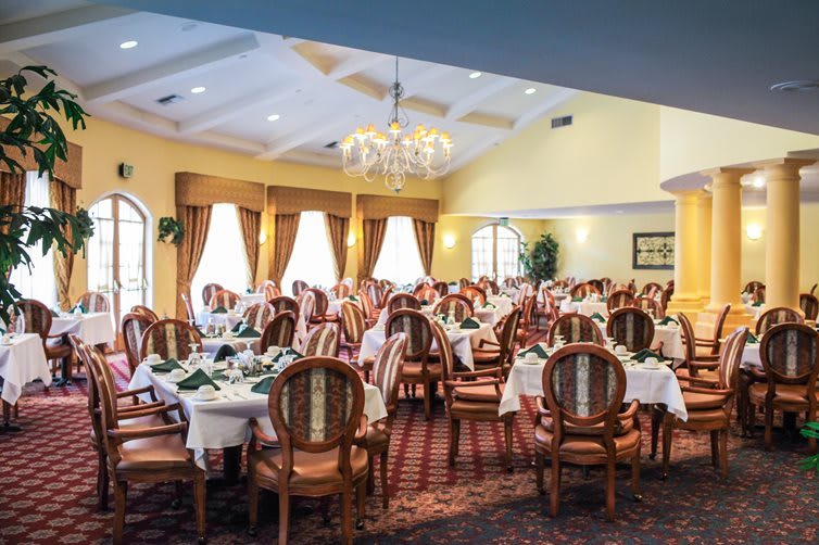 An elegantly decorated dining room with neatly arranged tables and chairs, featuring a chandelier and large windows.