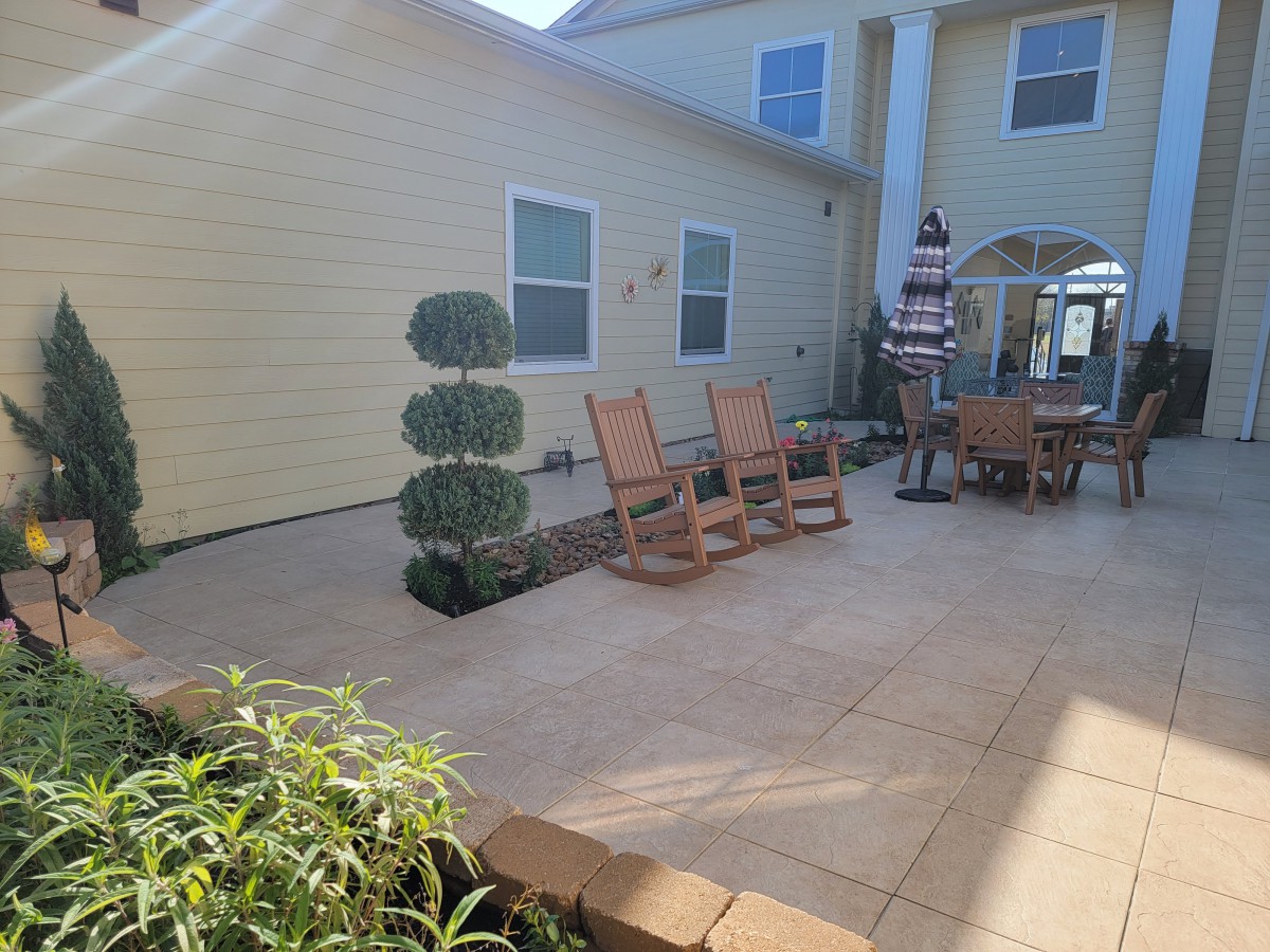 A sunny patio with rocking chairs, a table, and lush greenery.