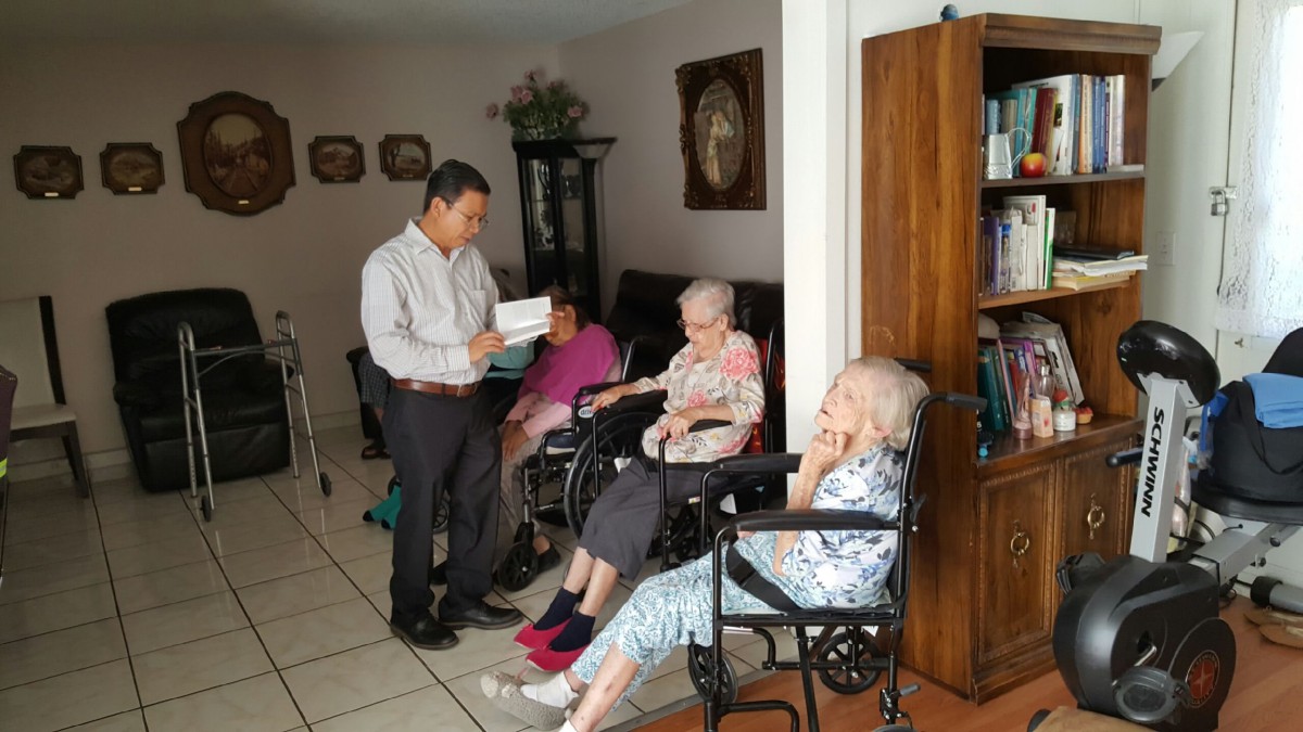 A man engages with elderly women in wheelchairs at a care home.