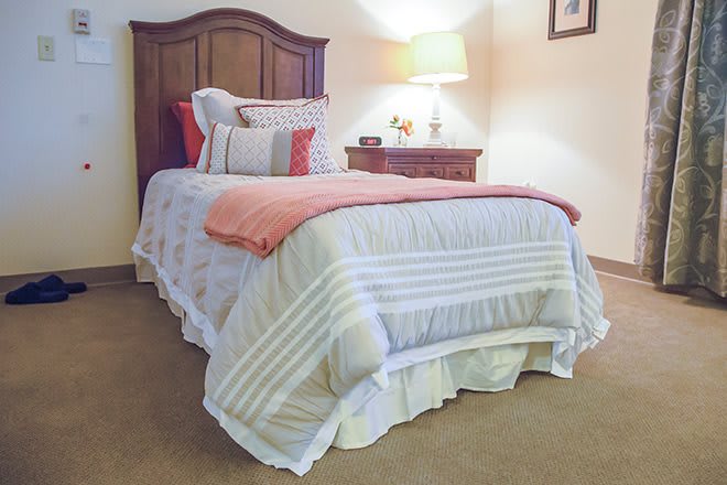 A cozy bedroom setup with a neatly made bed, nightstand, and lamp.
