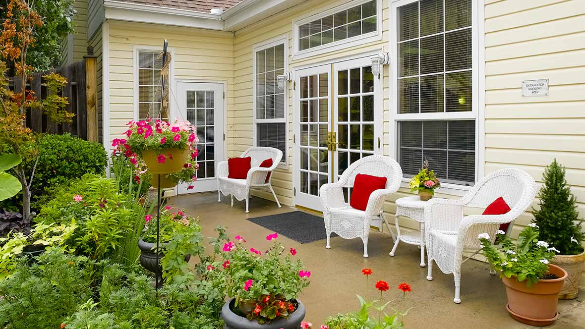 A cozy patio with white chairs and a table, surrounded by vibrant flowers.