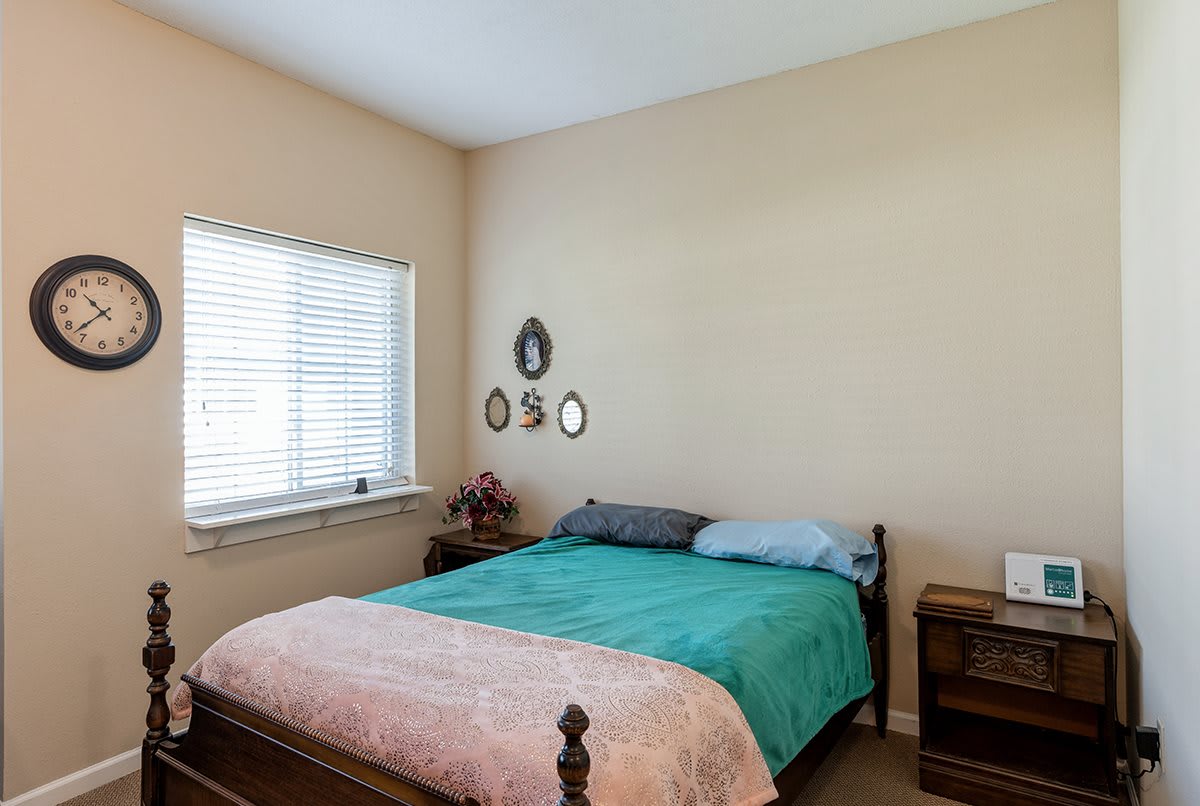 A cozy bedroom featuring a bed with colorful bedding, a window with blinds, and decorative wall art.