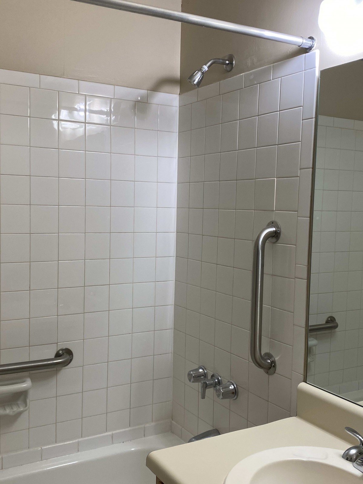 A bathroom featuring a tiled shower area with grab bars and a mirror.