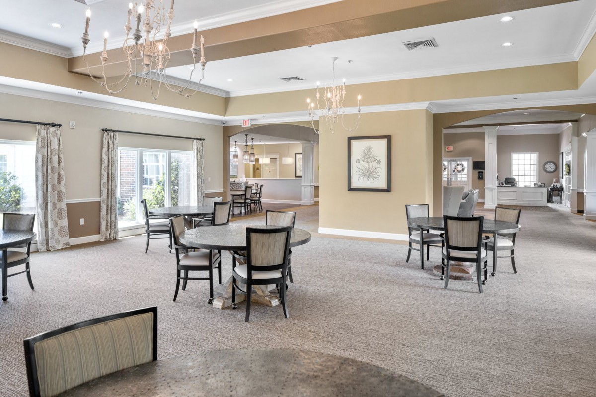 A spacious and elegantly designed dining area with multiple tables and chairs, featuring chandeliers and large windows.