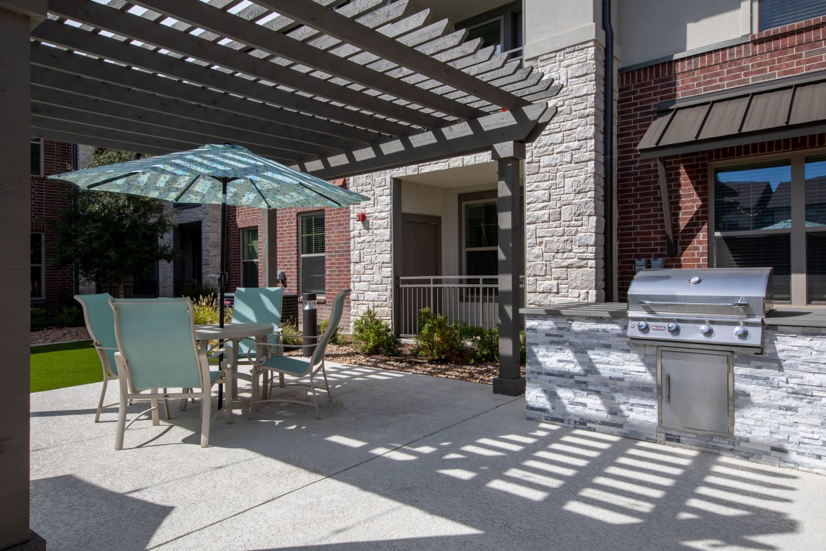 A sunny patio area with a pergola, outdoor seating, and a grill.