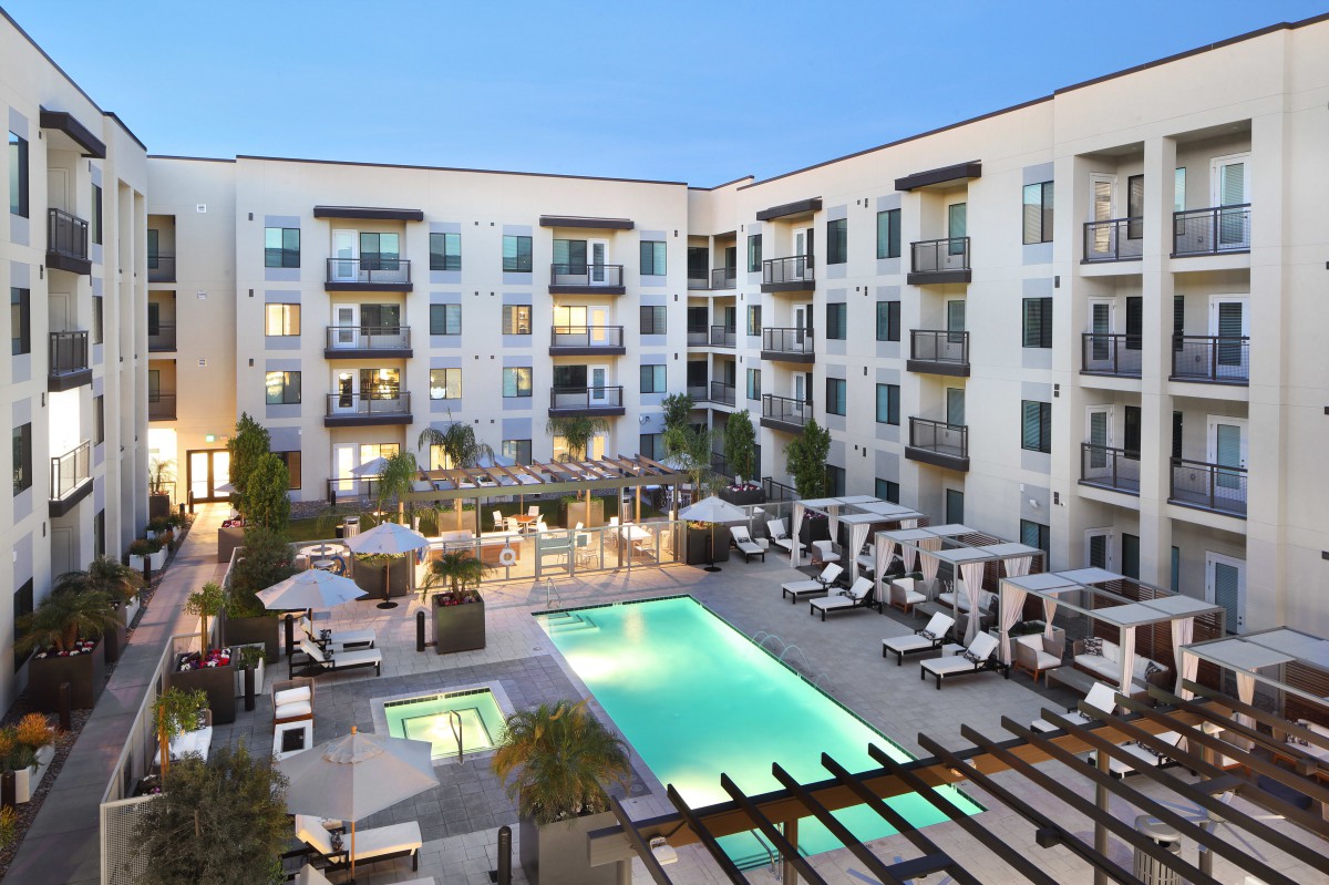 Modern apartment complex with a central swimming pool and outdoor seating area during the evening.