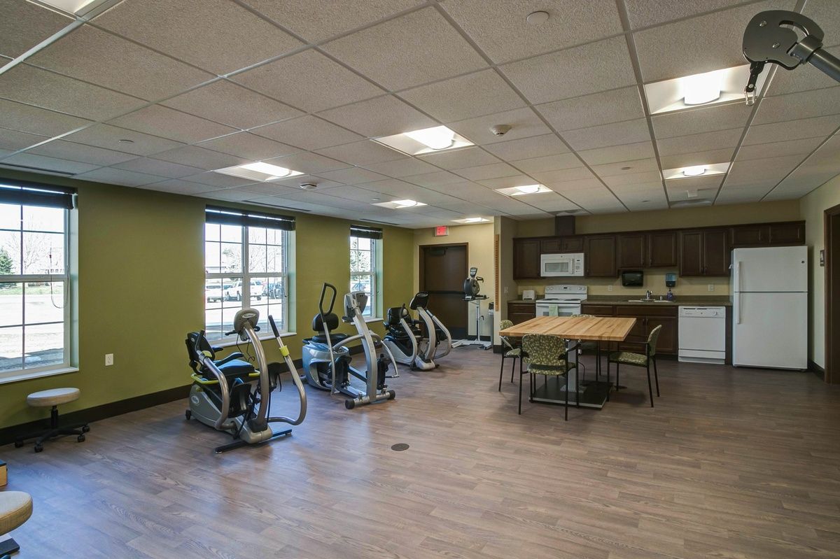 A spacious exercise room features stationary bikes, a kitchen area, and a table with chairs on a wooden floor.