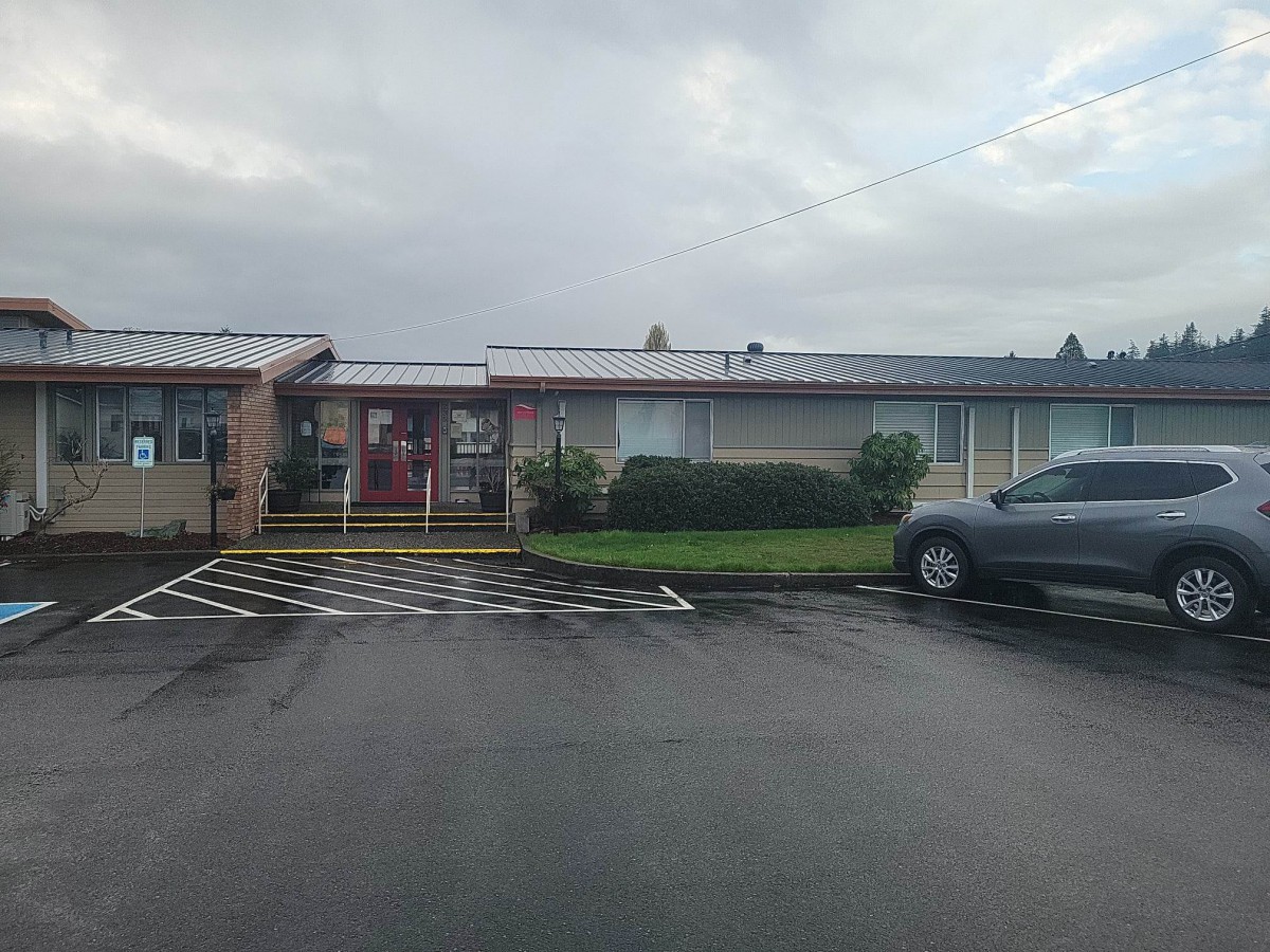 A single-story building with a car parked in an adjacent parking lot on a cloudy day.